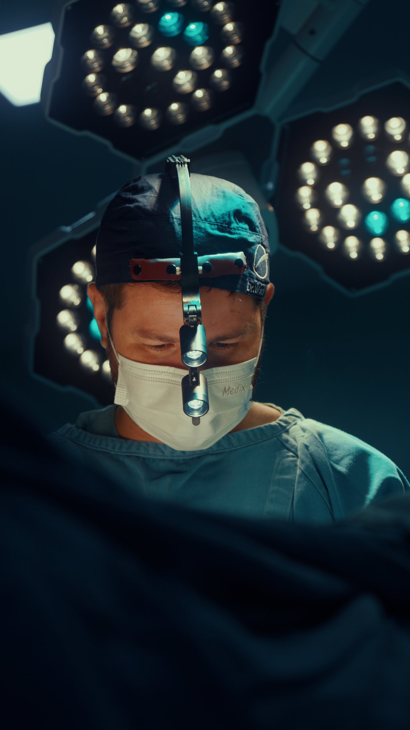 Dr. Warley em cirurgia, com lupa e focos cirúrgicos ao fundo